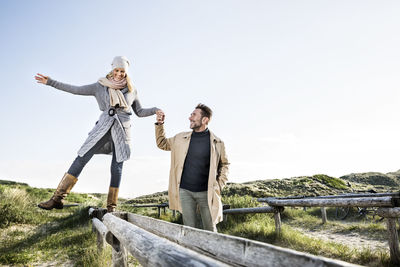 Man helping woman balancing on wooden stakes in dunes