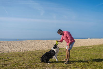 Bearded man playing with dog at beach in sunny day