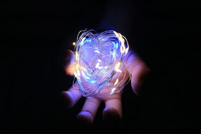 Close-up of hand holding illuminated light against black background