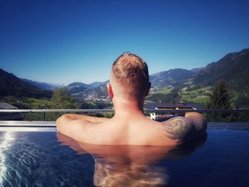 Rear view of shirtless man in swimming pool against blue sky