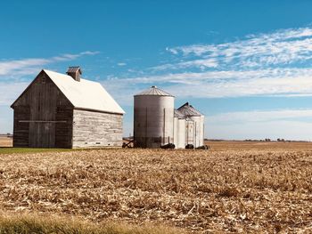 Barn on field by buildings against sky