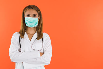 Portrait of female doctor standing against yellow background