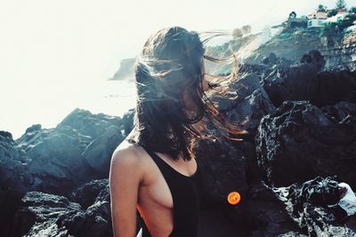 Sensuous woman with long hair standing by rocks at beach