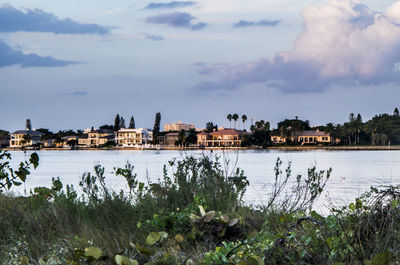 Houses by river against cloudy sky