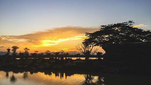 Silhouette trees by swimming pool against sky during sunset