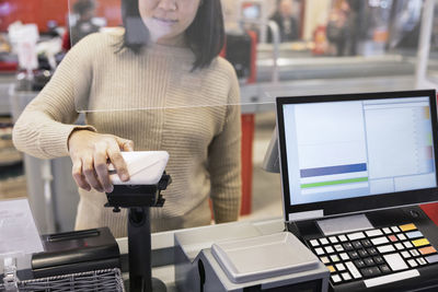 Midsection of young woman paying through smart phone at checkout counter in supermarket