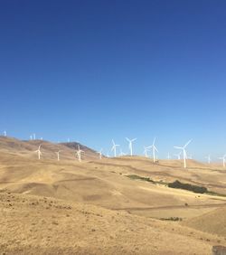 Windmills on landscape against clear blue sky