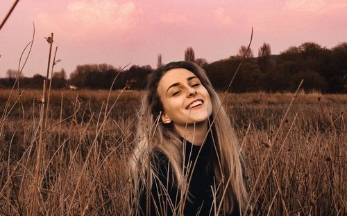 Portrait of smiling young woman on field against sky during sunset