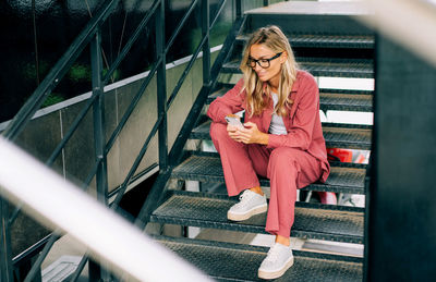 A young woman is browsing social media on her phone while sitting on the stairs.