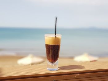 Close-up of drink on table at beach against sky