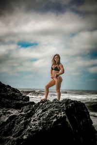 Full length of woman on rock at beach against sky