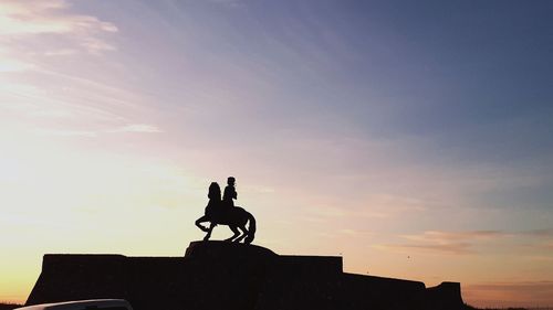 Silhouette man riding statue against sky during sunset