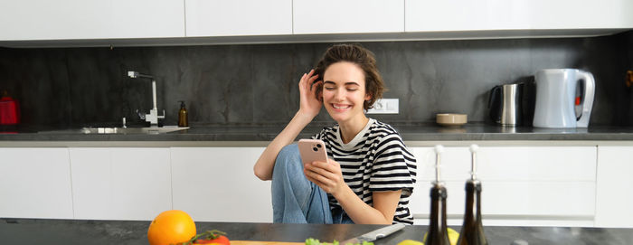 Portrait of smiling young woman using digital tablet in kitchen