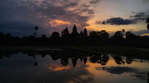 Scenic view of lake by buildings against sky during sunset