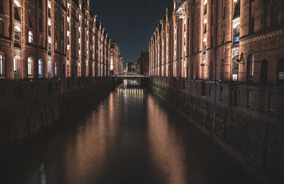 Bridge over canal amidst buildings in city at night