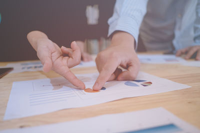 Midsection of businessmen pointing at document on table