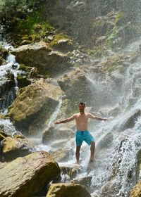 Full length of shirtless man standing on rocks in sea