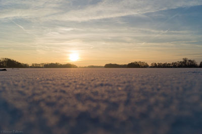 Snow covered field against sky during sunset