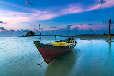 Boat moored on beach against sky during sunset