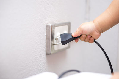 Cropped hand of boy inserting electric plug in electrical outlet at home