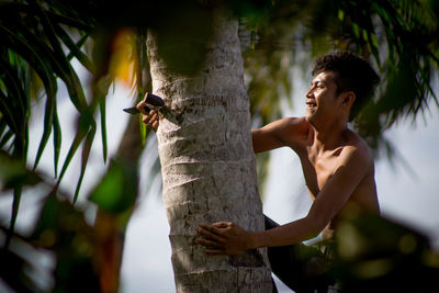 Full length of shirtless young man on tree trunk