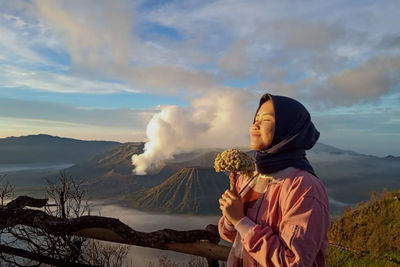 Young woman with eyes closed holding flowers on mountain