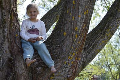 Portrait of cute girl sitting on tree trunk