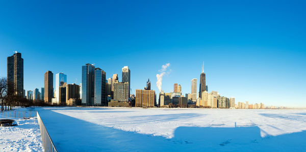 Modern skyscrapers by frozen lake michigan against blue sky