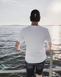 Rear view of man standing by railing looking at sea against sky