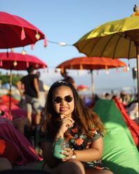 Portrait of woman holding drink while sticking out tongue at beach