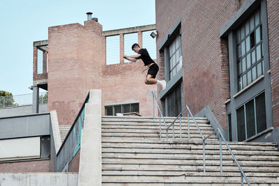 Side view of focused young male jumping over stone steps in city while doing parkour and showing trick