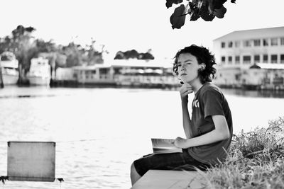 Side view of boy holding book while sitting on pier by lake