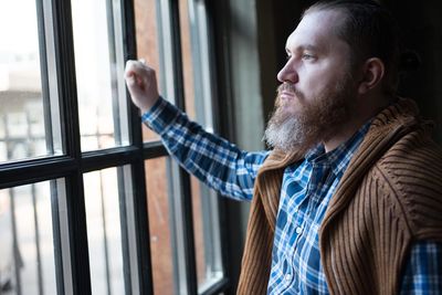 Thoughtful man wearing suspender looking through window at home