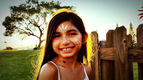 Portrait of girl with face paint by wooden fence against sky