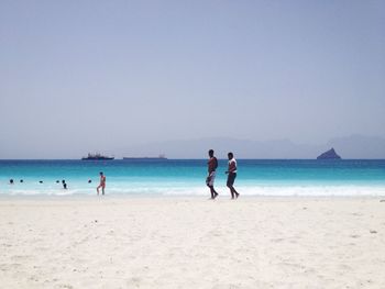 Silhouette friends walking at beach against clear sky