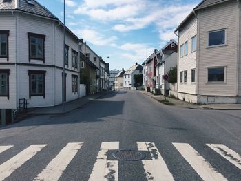 Empty road amidst buildings against sky during sunny day