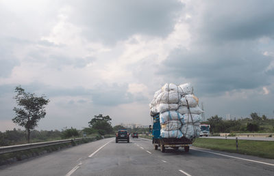 Vehicles on road against cloudy sky