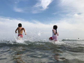 Rear view of men enjoying in sea against sky