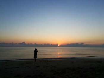 Silhouette man standing on beach against clear sky during sunset