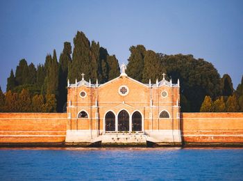 Building by river against clear blue sky - venice cemetery