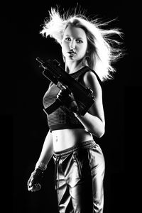 Portrait of young woman holding gun against black background