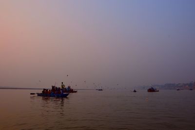 People in boat sailing on river against clear sky during sunset