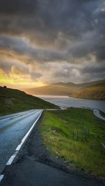Road amidst field against sky during sunset