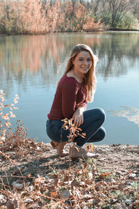 Portrait of smiling young woman sitting by lake