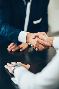 Midsection of business people giving handshake at desk in office