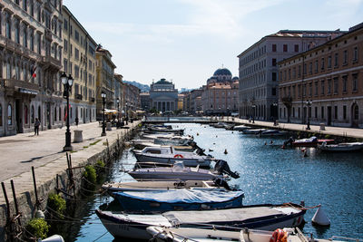 Boats moored on canal by buildings against sky