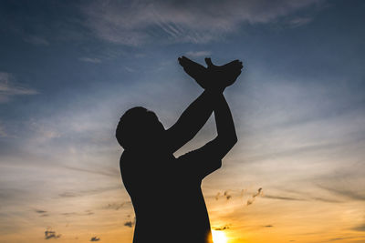 Silhouette man making bird with hands against sky during sunset