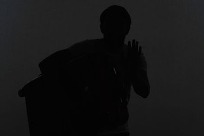 Rear view of silhouette man standing against dark background