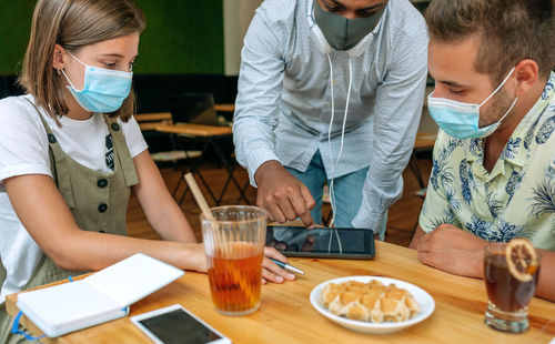 Cheerful friends wearing mask sitting at restaurant