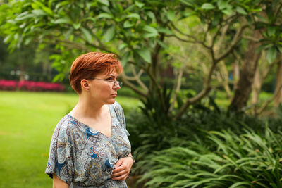 Young woman looking away while standing against trees